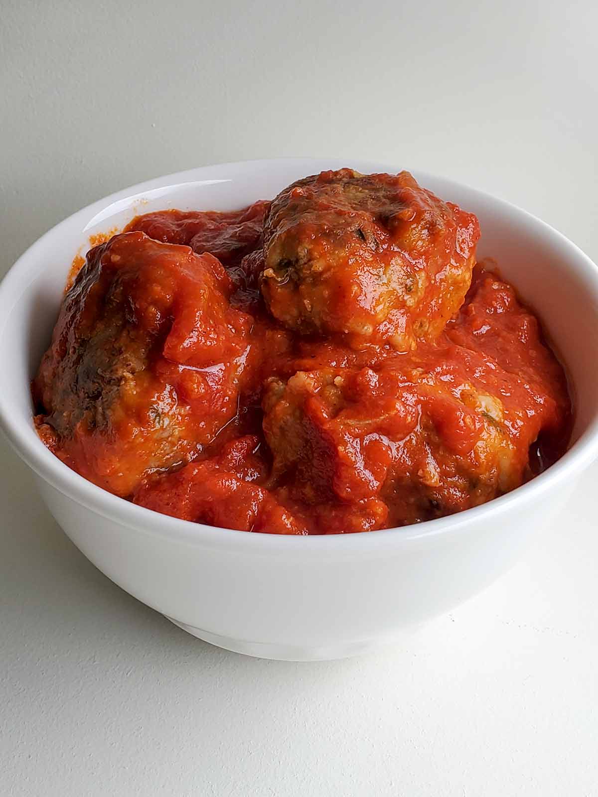 A white bowl filled with Italian-style meatballs and tomato sauce.