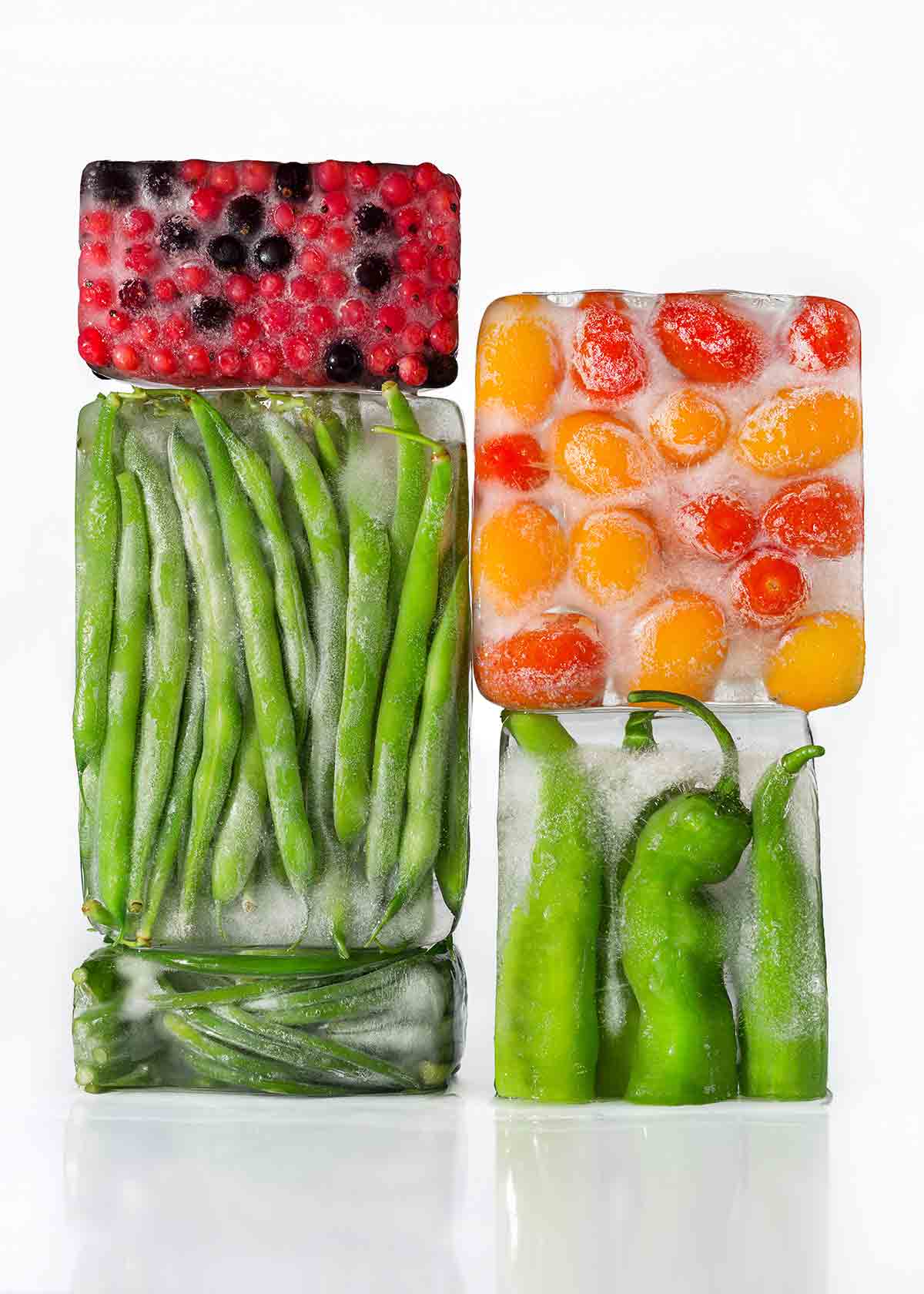 Four blocks of ice with berries, cherry tomatoes, green beans, and fava beans frozen inside