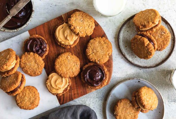 A cutting board covered with peanut butter-oatmeal sandwich cookies, some opened revealing their chocolate filling