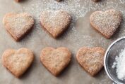 Seven Linzer heart cookies being dusted with confectioners' sugar