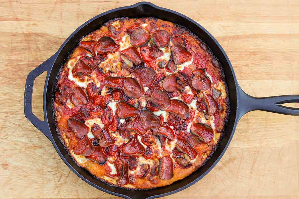 A whole skillet pepperoni pizza in a cast-iron skillet on a wooden surface