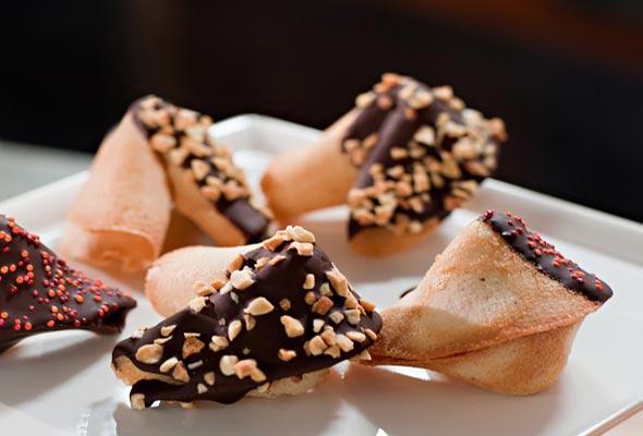 Five change your fortune cookies, coated with chocolate and nuts on a white platter.