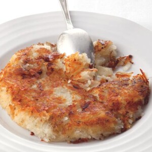 A cooked crisp potato cake on a white plate with a spoon resting in the potato cake.